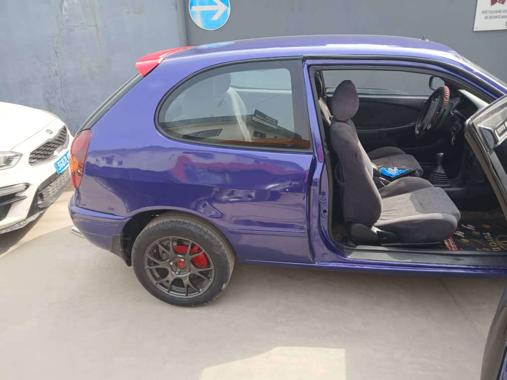 Toyota Etio Compact bleu violet vue de profil côté gauche, jantes en alliage, vitres latérales propres, ligne de caisse complète mise en valeur.